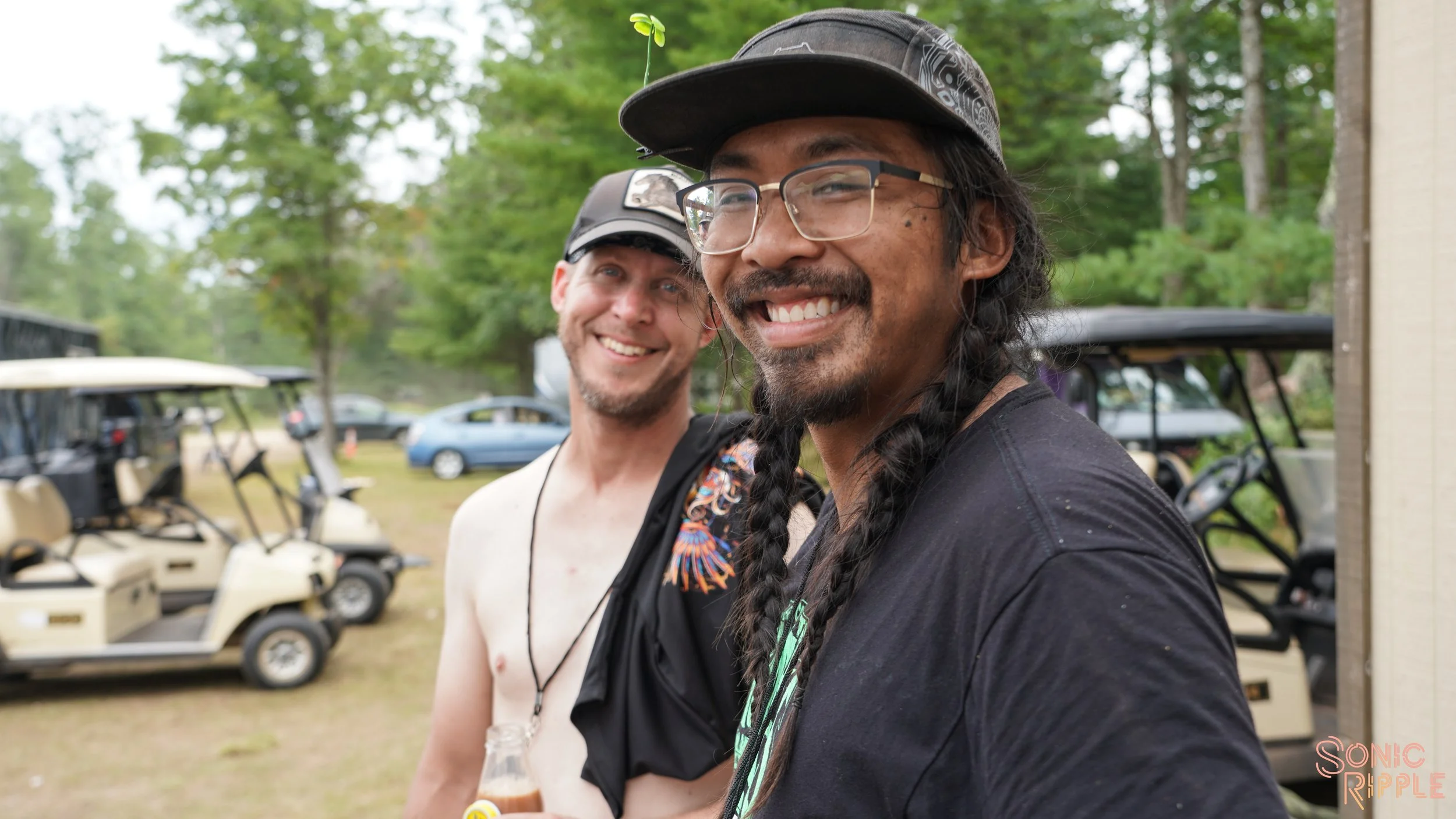 Two smiling men near golf carts in wooded area