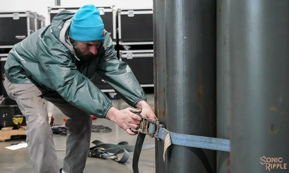 Man securing large cylindrical metal objects with blue strap